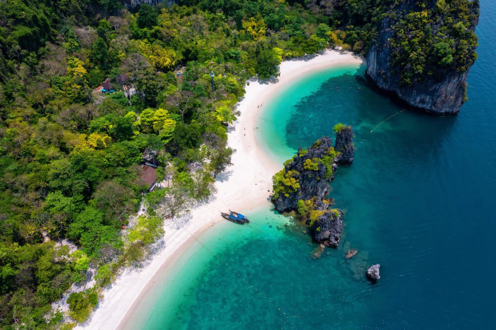 Aerial view of a tropical beach with lush greenery and clear turquoise waters, inviting you to become a Travel Agent.