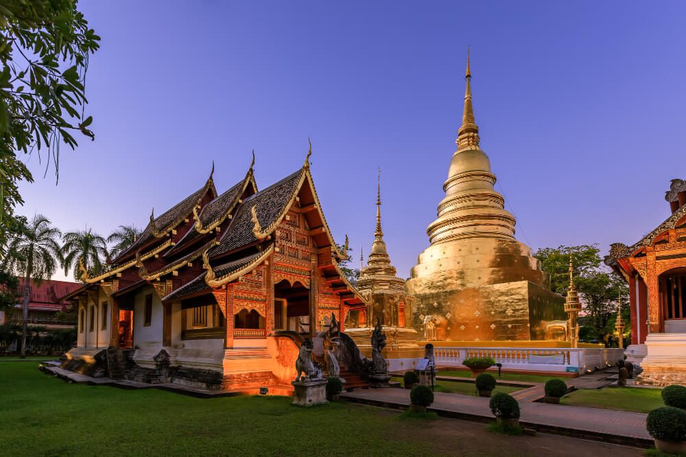 Traditional Thai temple complex with golden stupa at sunset, presented by our travel agency.