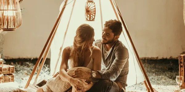 A couple on their honeymoon sitting closely together under a makeshift tent, engaging in a tender moment.