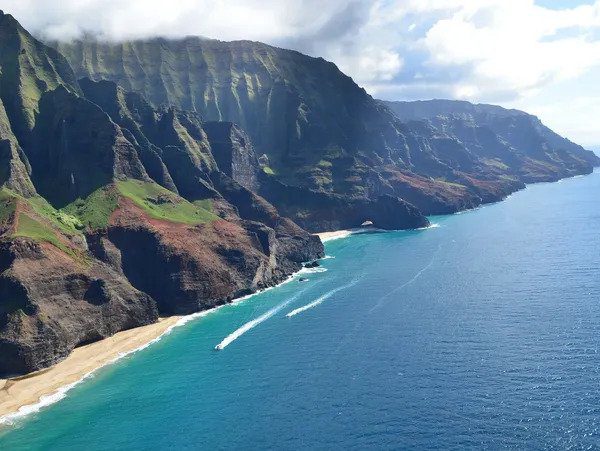 Aerial view of a rugged coastline with cliffs, a sandy beach, and clear blue waters. Hire a Travel Agent to explore this paradise.