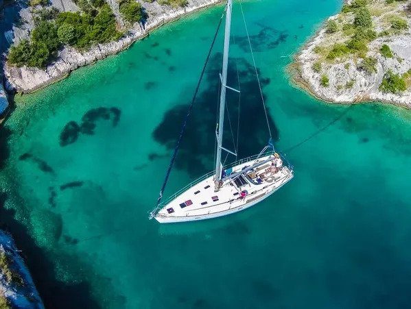 A sailboat anchored in the clear, turquoise waters near a rocky coastline. Consider hiring a travel agent to explore this majestic setting.