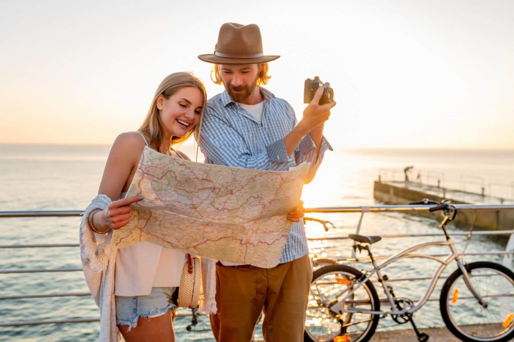 Two honeymoon travelers consulting a map by the seaside at sunset, with bicycles in the background.