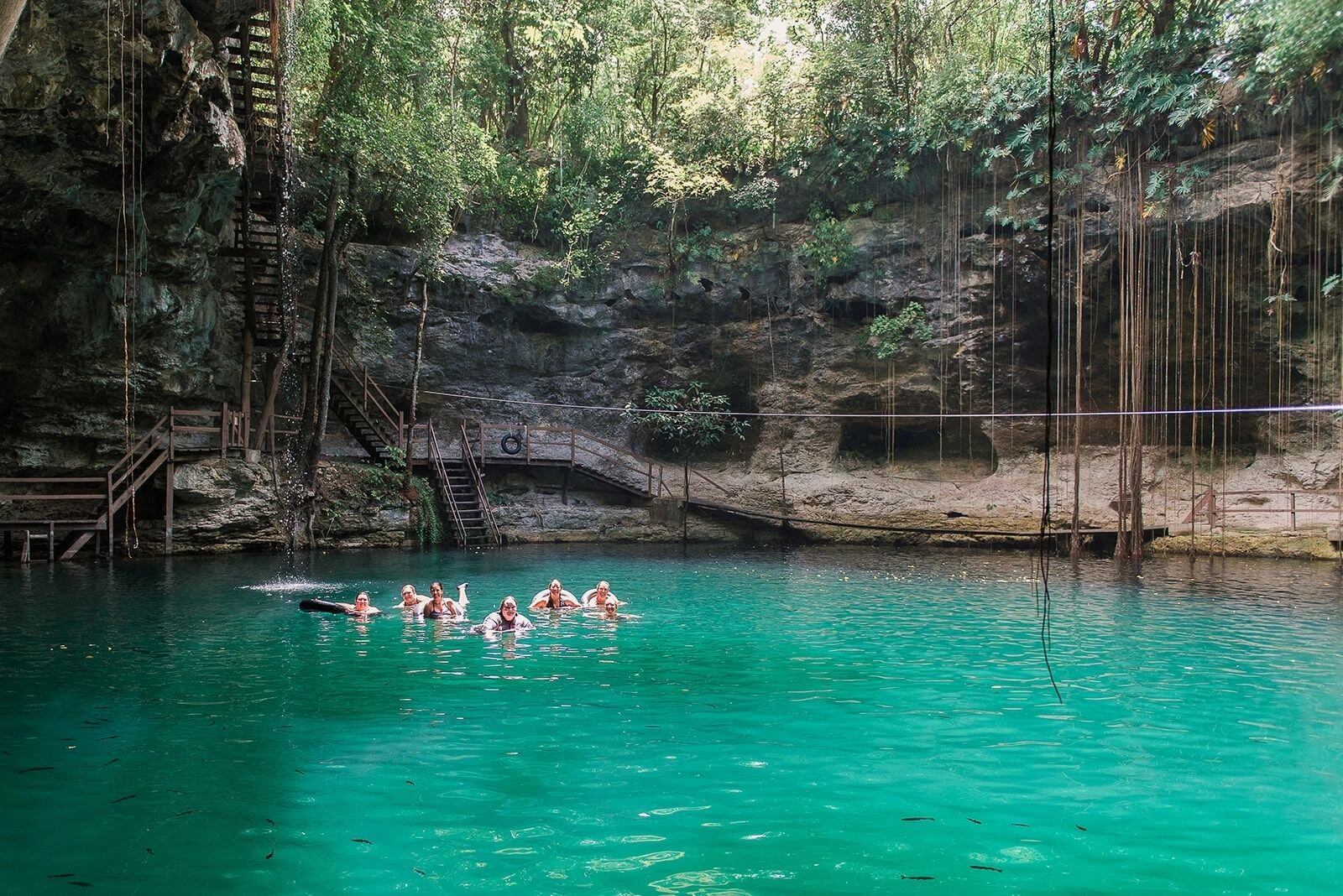 Tourists enjoying a swim in a serene cenote with natural rock walls and vegetation.