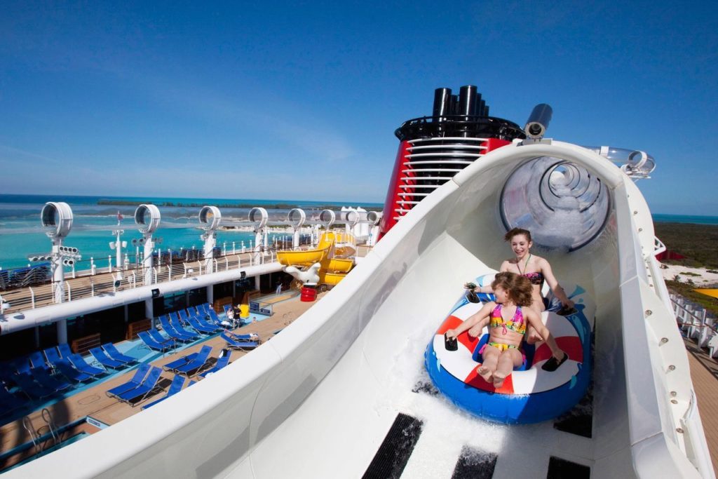 Two individuals enjoying a water slide on the deck of a cruise ship with the ocean in the background.