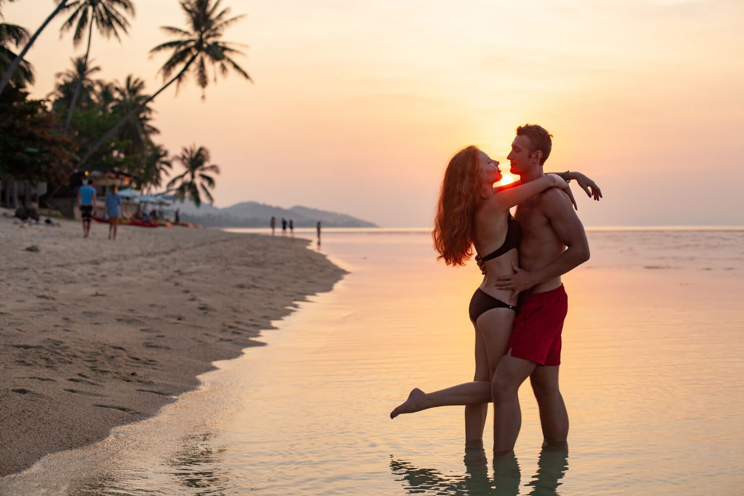 A honeymoon couple embracing on a beach at sunset