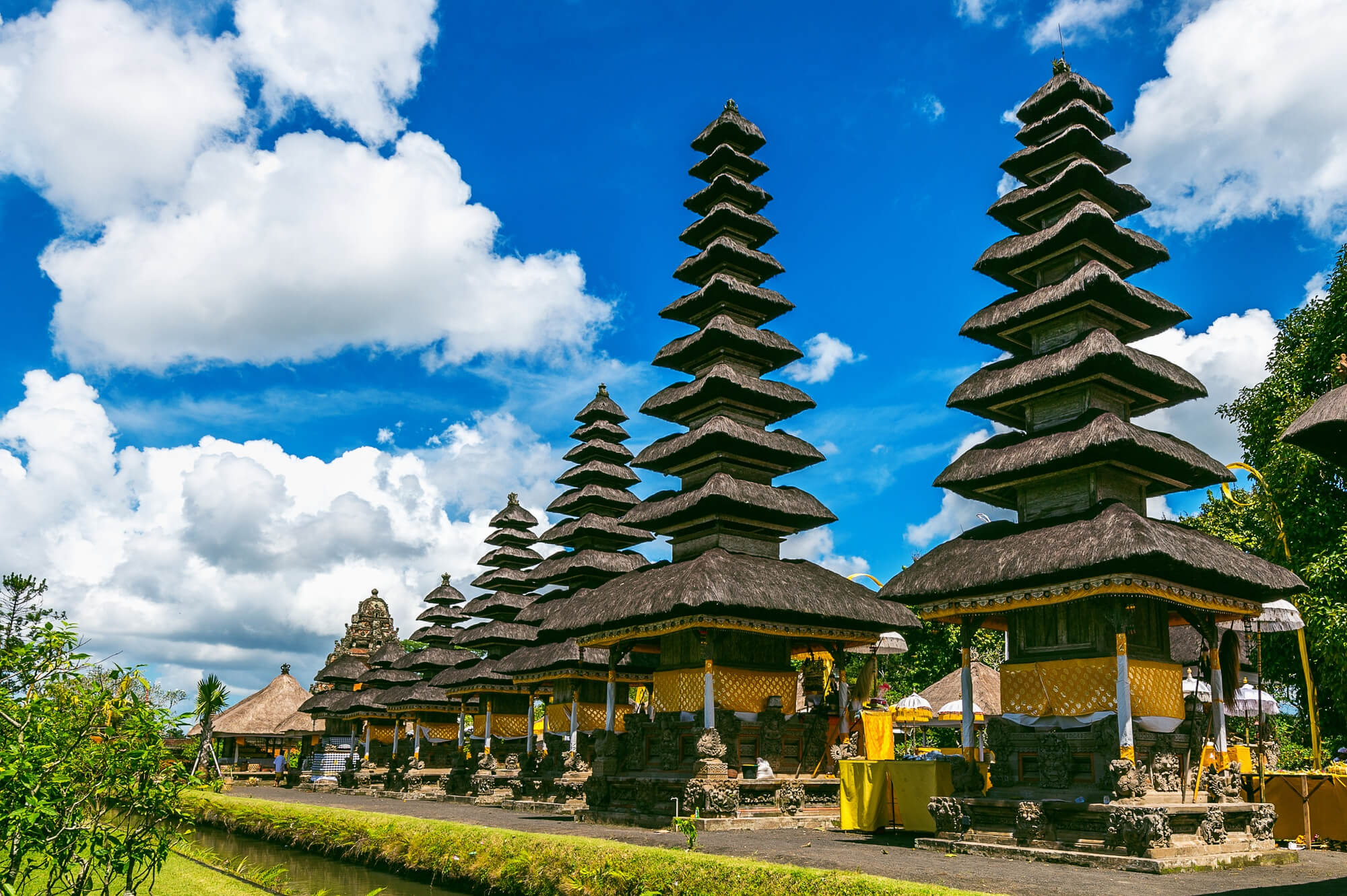 Traditional balinese temple with multi-tiered pagodas under a blue sky with clouds, presented by our travel agency.