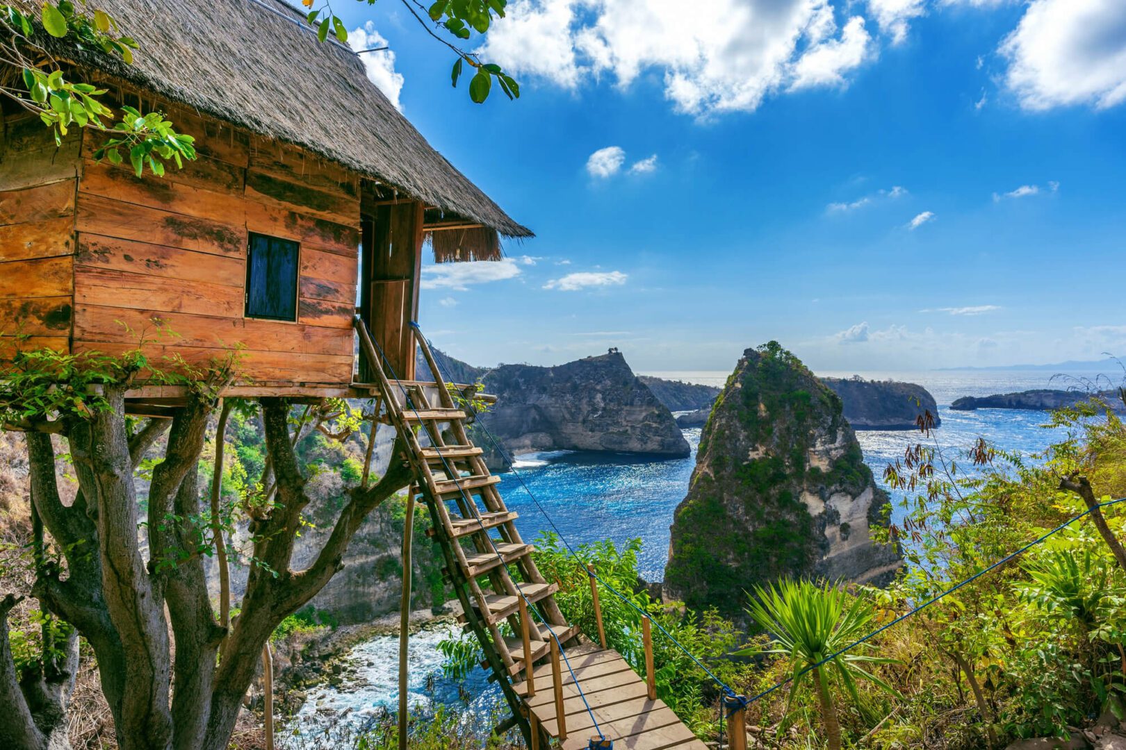 Travel agency offers a wooden cabin perched on a cliff overlooking the ocean with a scenic view of rock formations.