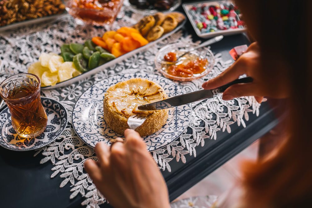 A person spreads jam on a round piece of bread at a table set with various foods and tea.