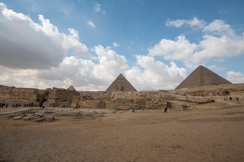 The giza pyramid complex under a cloudy sky with tourists visiting the ancient site.