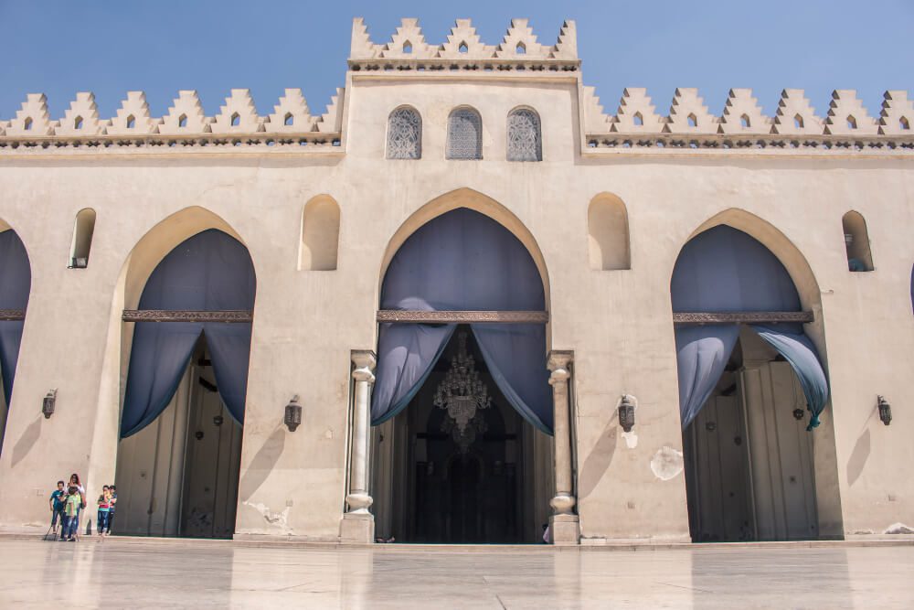 Facade of a traditional building with arched doorways and ornamental detailing, under a clear blue sky.