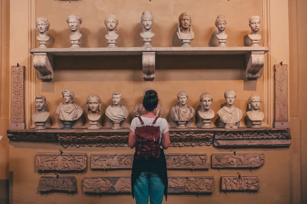 Visitor observing a collection of ancient busts on display at a museum.