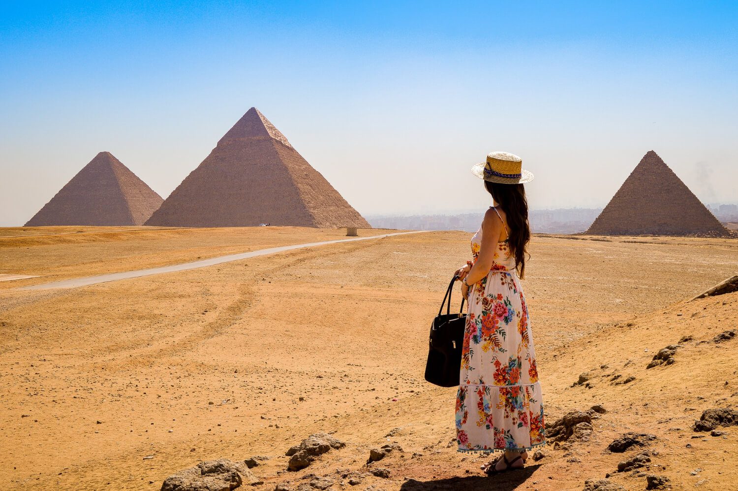 Woman in a floral dress and hat observing the great pyramids of giza on a clear day.