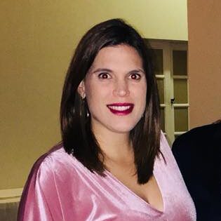A travel expert with shoulder-length hair, red lipstick, and a pink satin top, smiling at the camera.