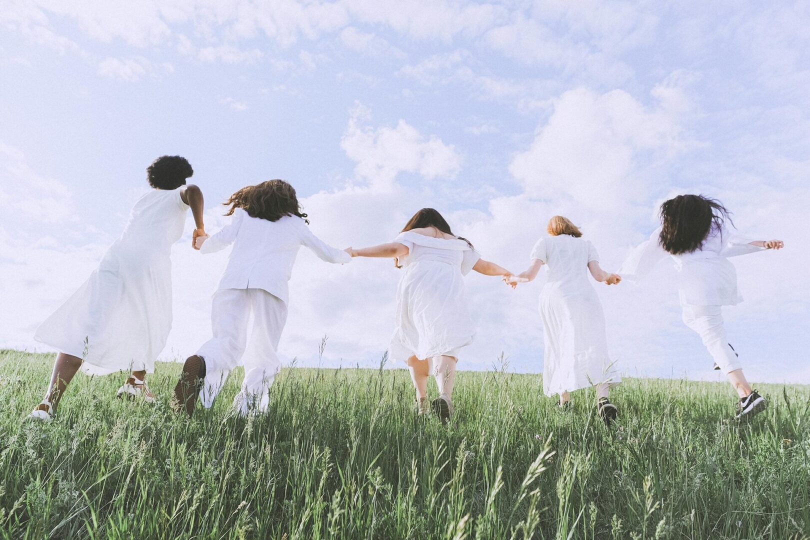 A family in white running together across a grassy hill