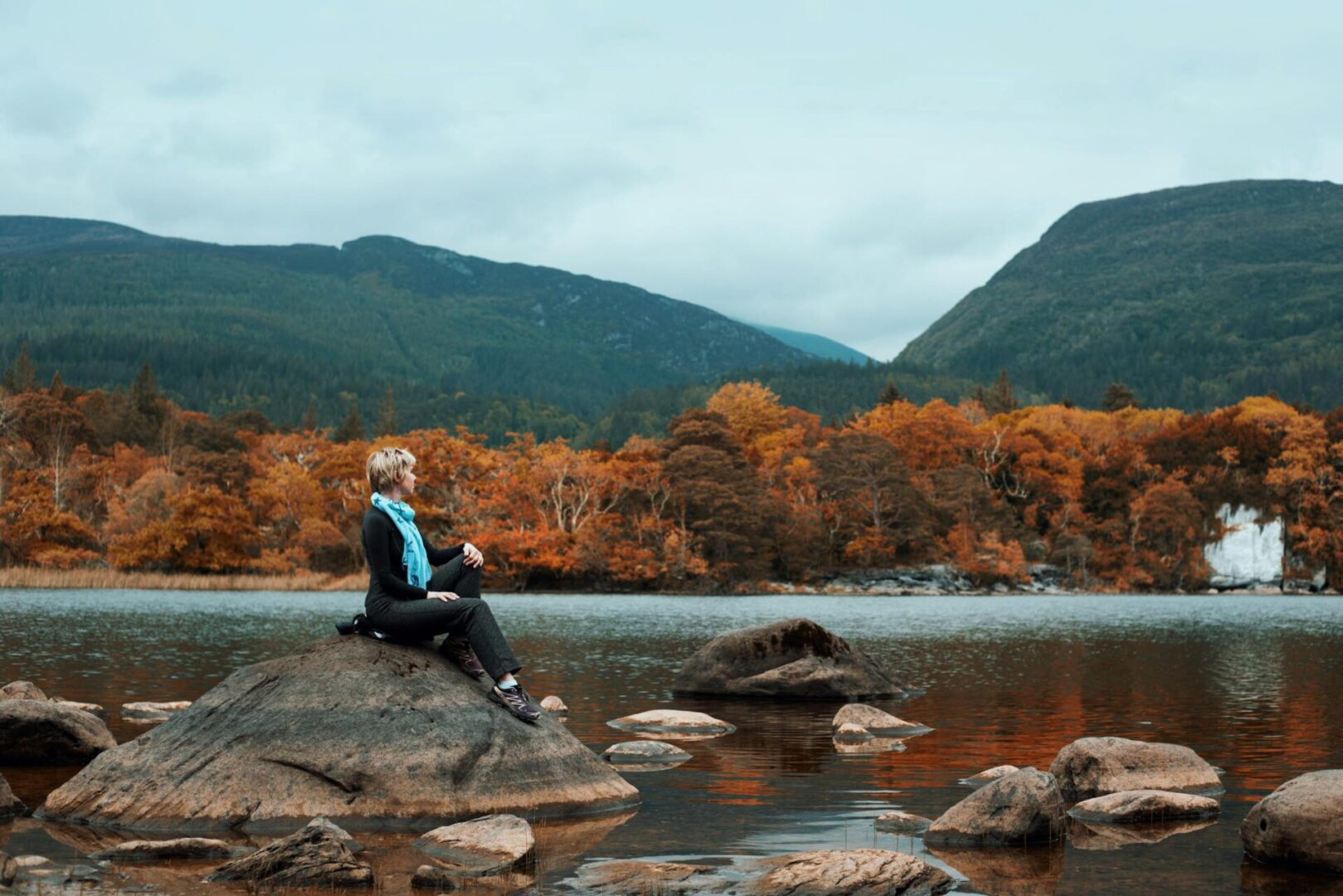 A traveler sitting by a lake among autumn trees and mountains in Ireland