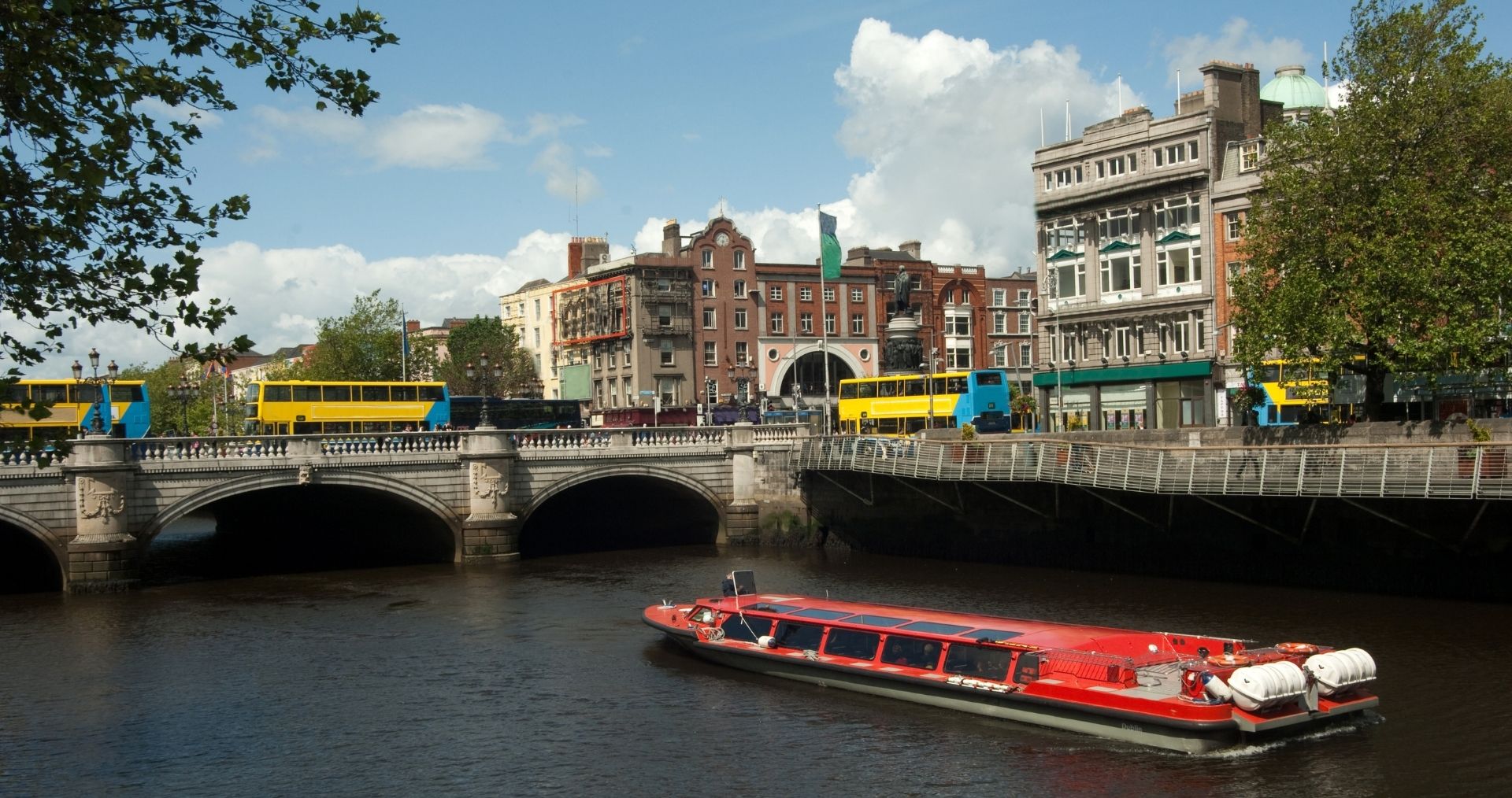 A red tour boat on the River Liffey in Dublin beside a stone bridge