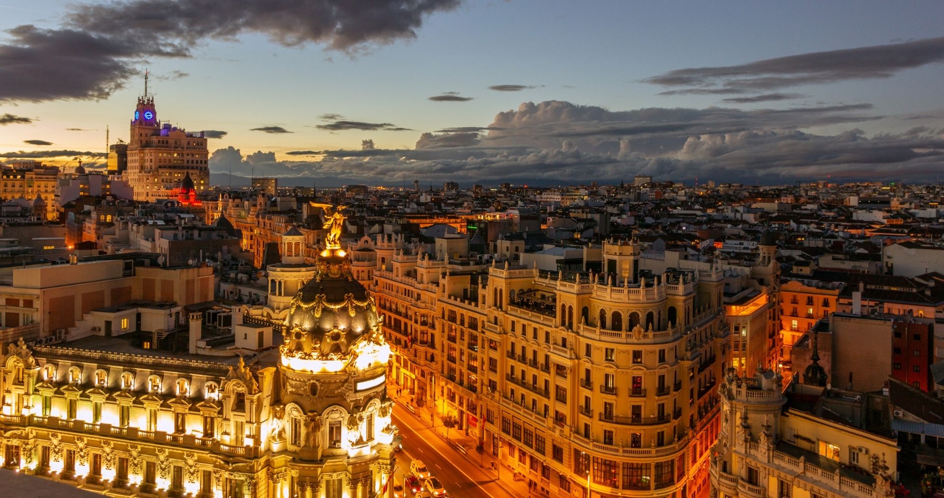 Madrid’s Gran Vía lit up at dusk beneath a dramatic sky