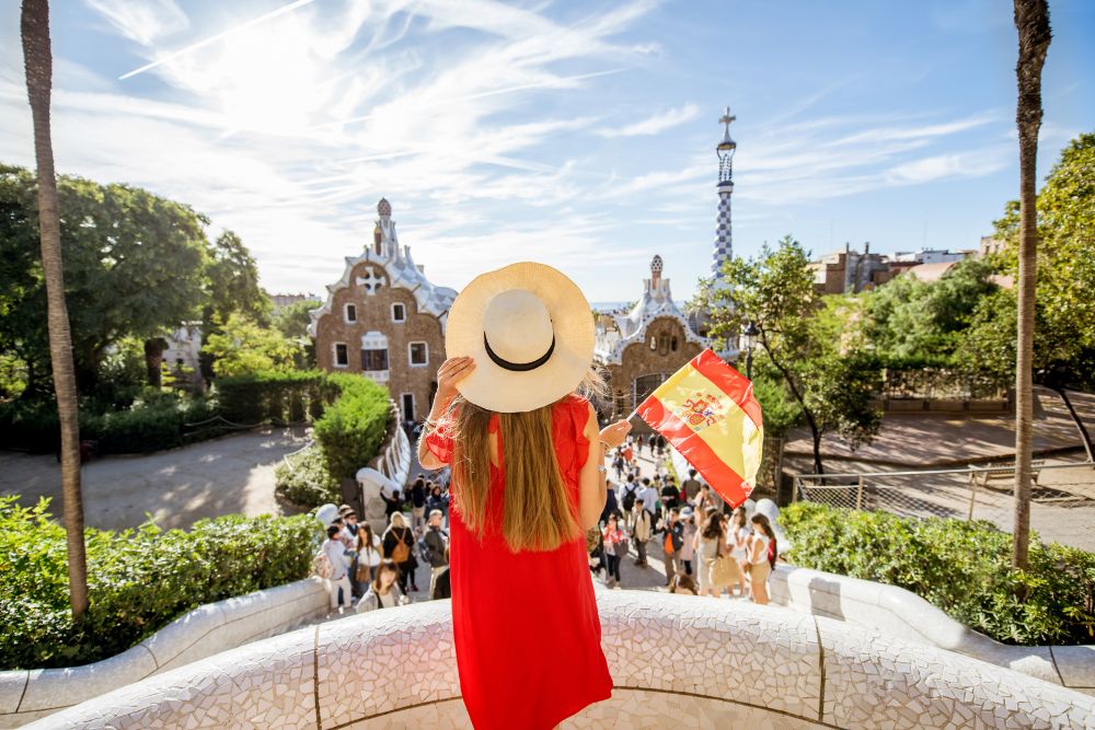 A traveler in a sun hat holding a Spanish flag at Park Güell