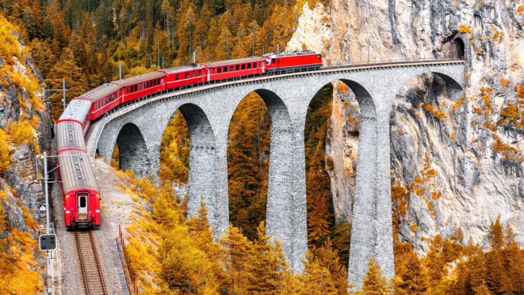 A red train crossing a curved stone viaduct in the Swiss Alps