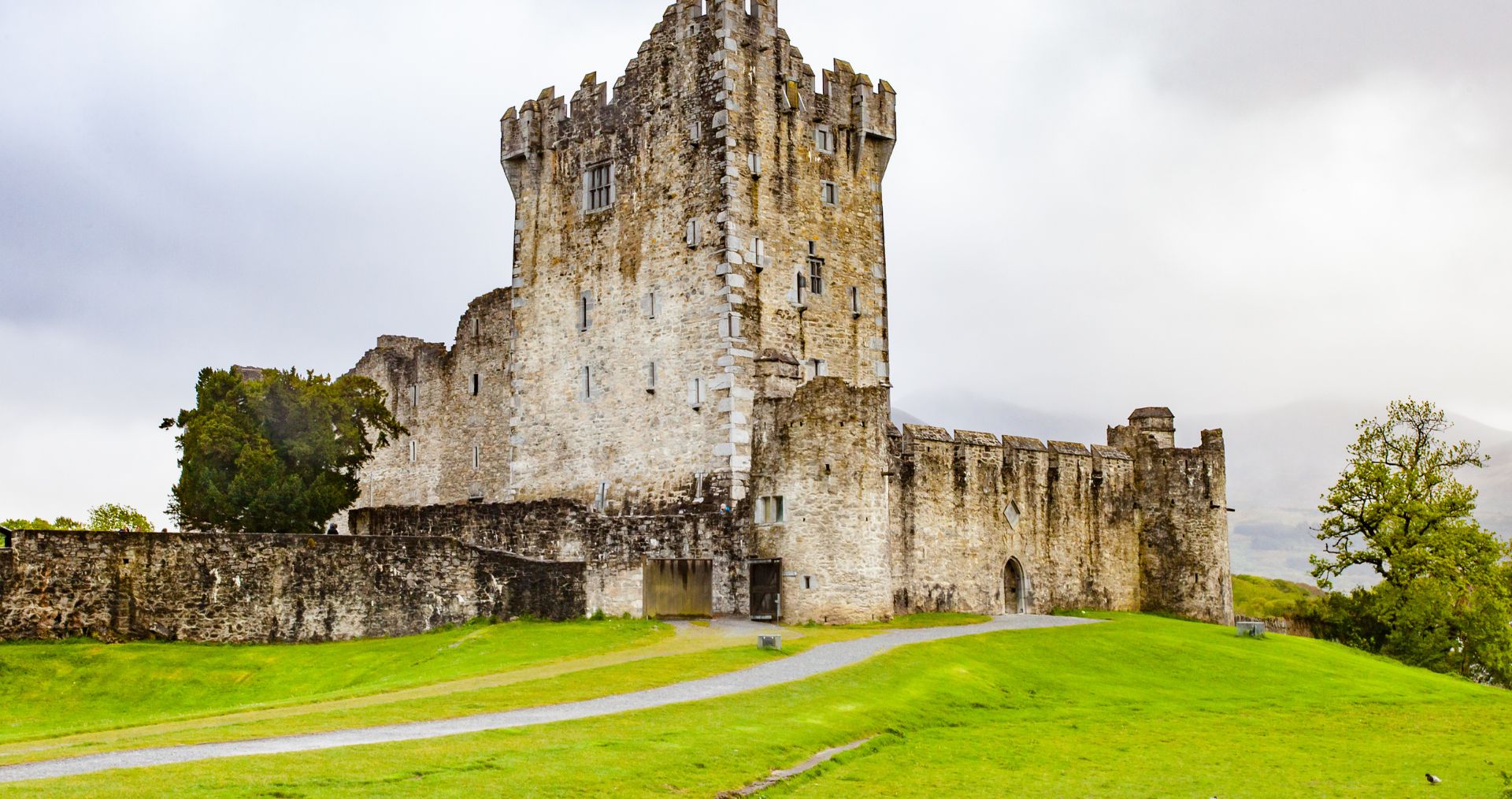 The stone tower house of Ross Castle on a green lawn in County Kerry