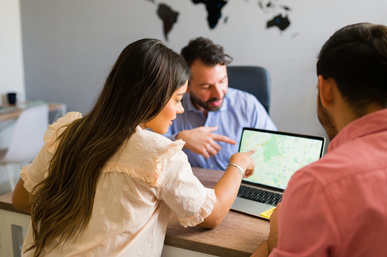 Travel advisor planning a trip with a couple on a laptop map