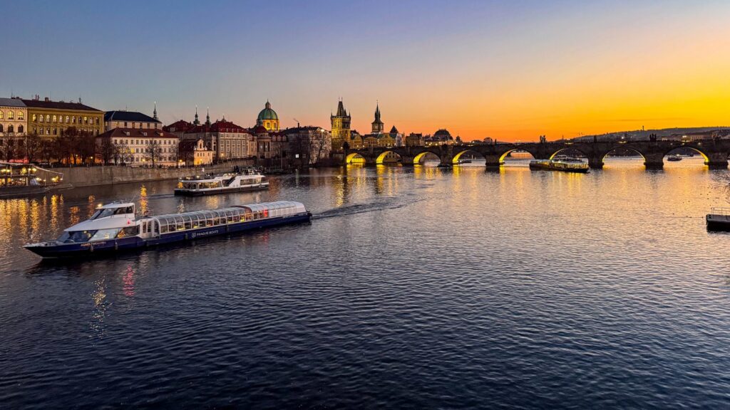 A river cruise ship at sunset beside a historic European city