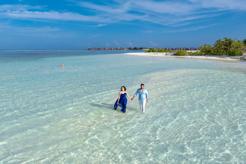 Couple wading across a clear turquoise sandbar