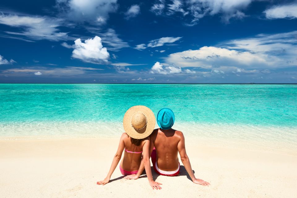 Couple in sun hats sitting on a white-sand beach