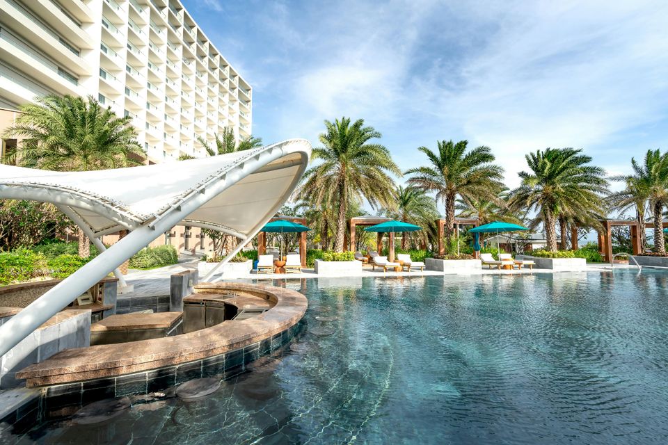 Palm-lined resort pool beside a beachfront hotel