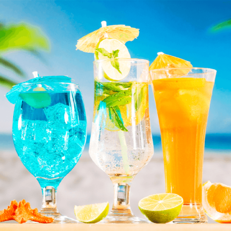 Colorful tropical drinks on a beach with a blue sky in the background, showcasing why use a travel agent for your idyllic vacation.