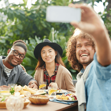 Three friends taking a selfie at an outdoor dining table, showcasing why using a travel agent for unique experiences is beneficial.