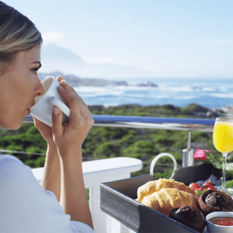 Woman enjoying breakfast with a view of the ocean, contemplating why use a travel agent for her next adventure.